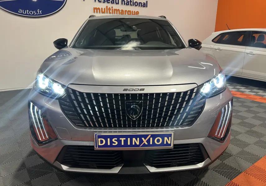 Vue frontale d'un Peugeot 2008 gris 2025 avec phares allumés et calandre noire distinctive en concession.