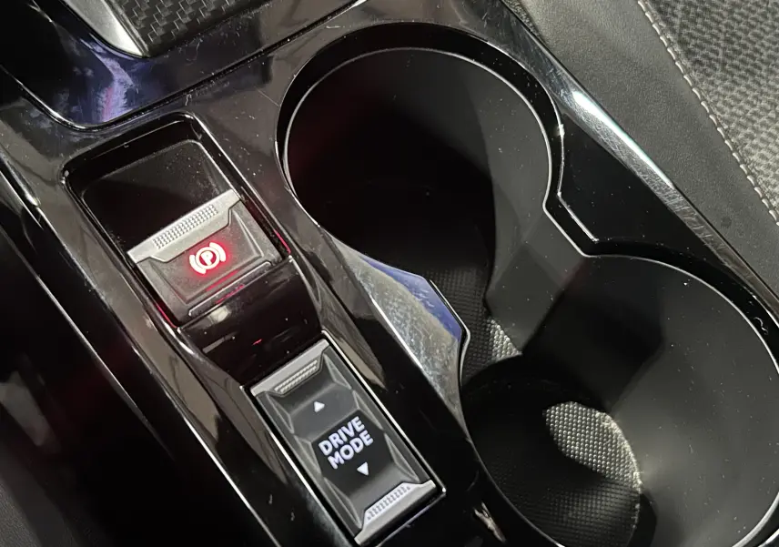 Gros plan sur la console centrale noire du Peugeot 2008 Allure Hybrid 145, avec bouton frein à main électronique et sélection drive mode.