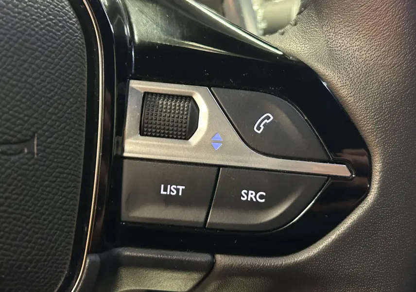 Gros plan sur les commandes noires et grises du volant du Peugeot 2008 gris hybride, avec boutons LIST, SRC et téléphone.