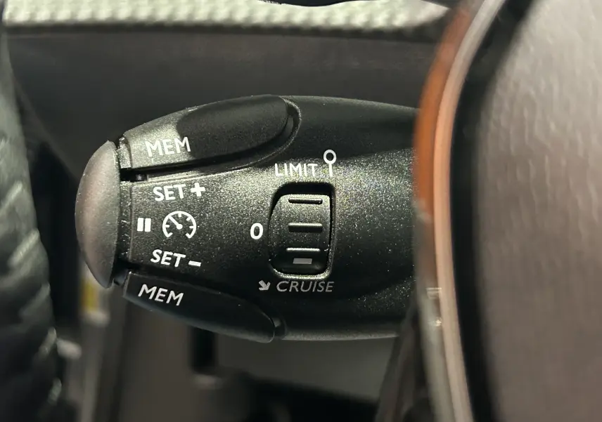 Gros plan sur la commande de régulateur de vitesse du Peugeot 2008 Allure Hybrid 145 gris, côté gauche du volant.