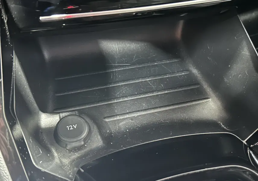 Prise 12V en gros plan dans la console centrale noire du Peugeot 2008 Allure Hybrid 145 e-DSC6 gris 2025.