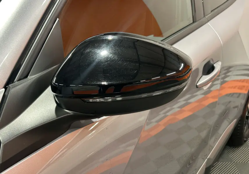 Rétroviseur noir brillant côté gauche du Peugeot 2008 Allure Hybrid 145 gris, avec poignée de porte visible.