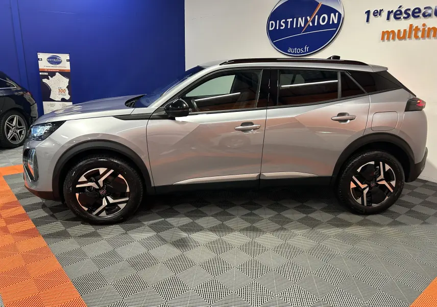 Profil droit d'un Peugeot 2008 Allure Hybrid 145 gris 2025 avec jantes noires et toit noir en showroom intérieur.