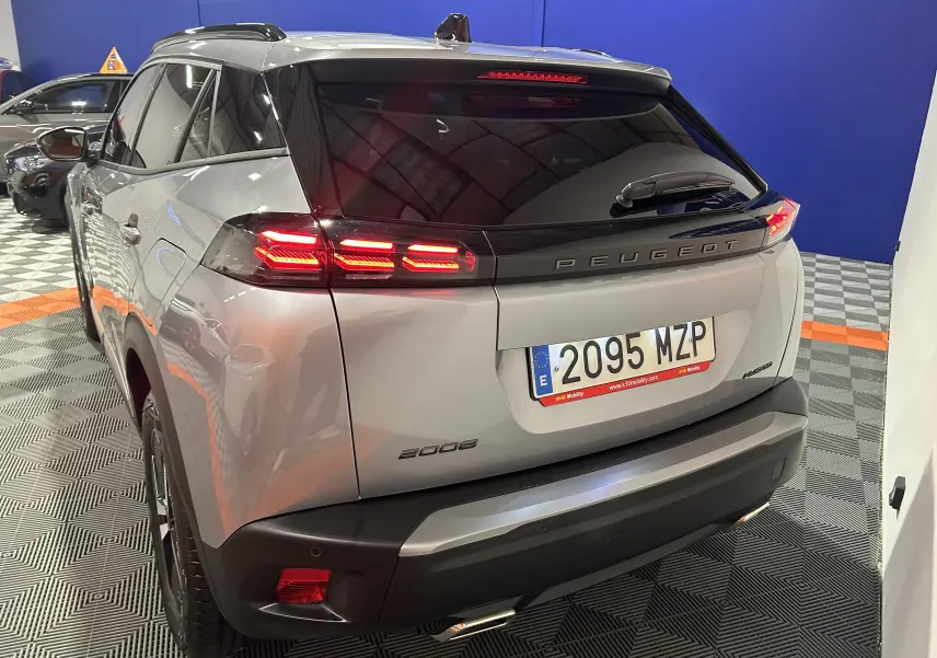 Vue 3/4 arrière droite d'un Peugeot 2008 gris hybride avec feux arrière LED allumés en intérieur showroom.