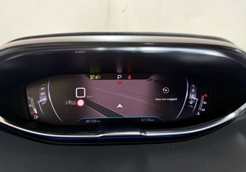 Vue rapprochée du tableau de bord numérique du Peugeot 5008 gris clair, affichant la navigation et les indicateurs de vitesse et température.