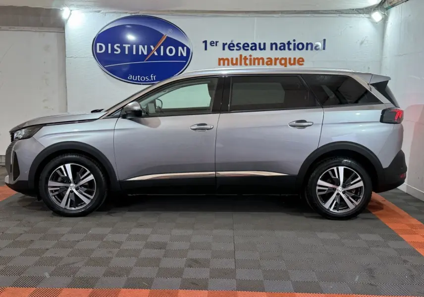 Vue de profil côté gauche d’un Peugeot 5008 gris clair avec jantes alliage et vitres teintées en intérieur showroom.