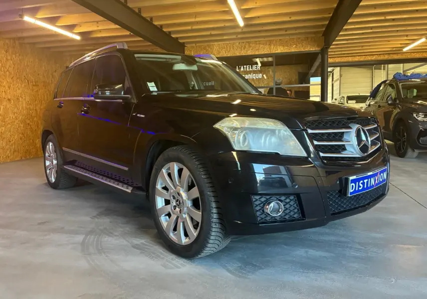 Mercedes GLK noir en 3/4 avant droit dans un garage, avec jantes alliage et calandre chromée visible.