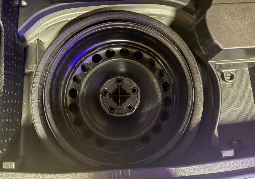 Vue rapprochée de la roue de secours noire en acier dans le coffre d’un Mercedes GLK 220 CDI noir de 2012.