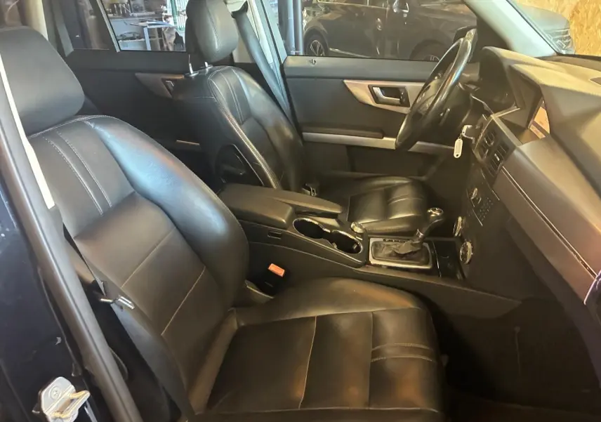 Vue intérieure côté conducteur du Mercedes GLK 220 CDI noir de 2012 avec sièges cuir noir et console centrale visible.