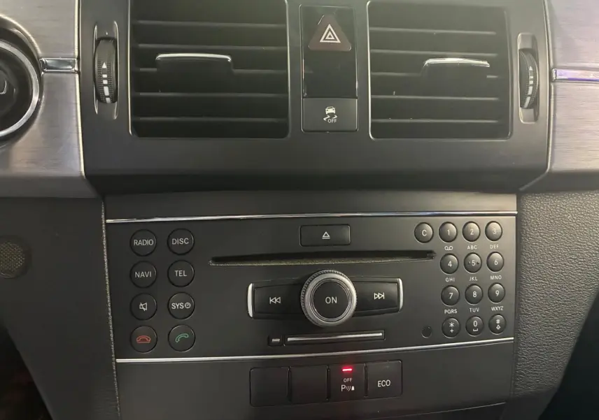 Vue rapprochée de la console centrale noire du Mercedes GLK 2012 avec commandes radio, climatisation et boutons de sécurité.