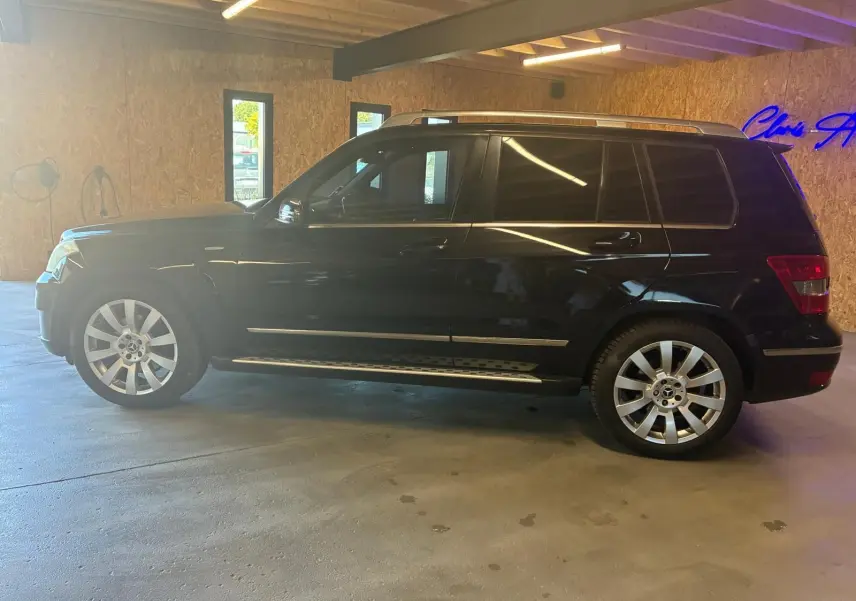 Vue de profil côté gauche d'un Mercedes GLK noir 2012 avec jantes alliage et barres de toit argentées.
