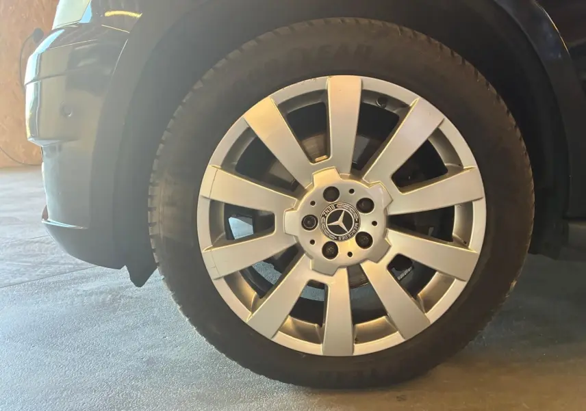 Gros plan sur la roue avant droite d’un Mercedes GLK noir, avec jante argentée à dix branches et logo central.