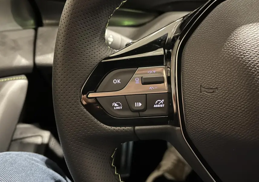 Gros plan sur le côté gauche du volant cuir perforé de la Peugeot 308 GT 2024 avec commandes de régulateur et limiteur.
