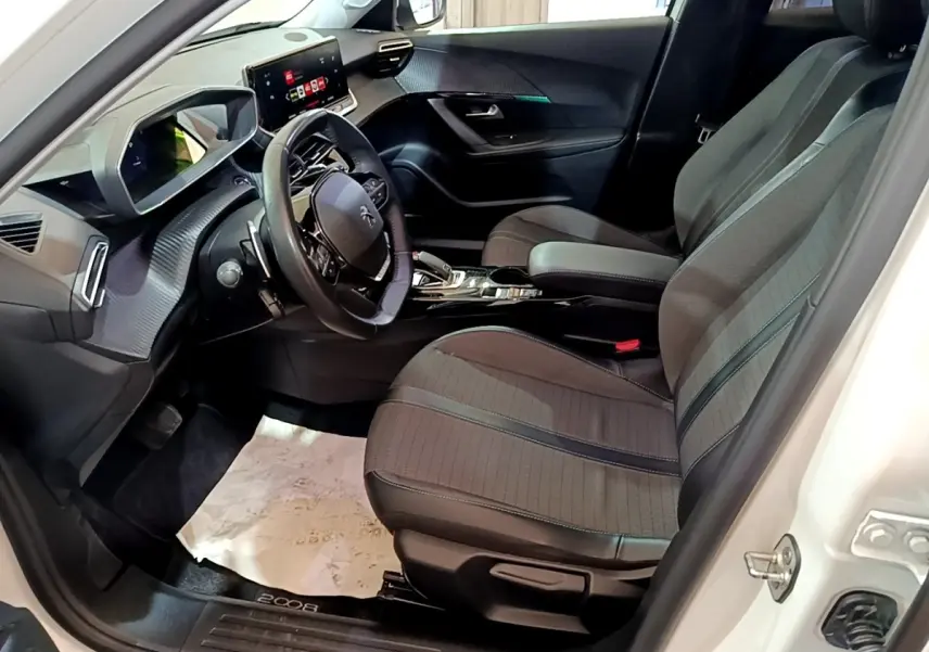 Vue intérieure côté conducteur du Peugeot 2008 blanc, mettant en valeur le volant cuir multifonctions et la console centrale moderne.