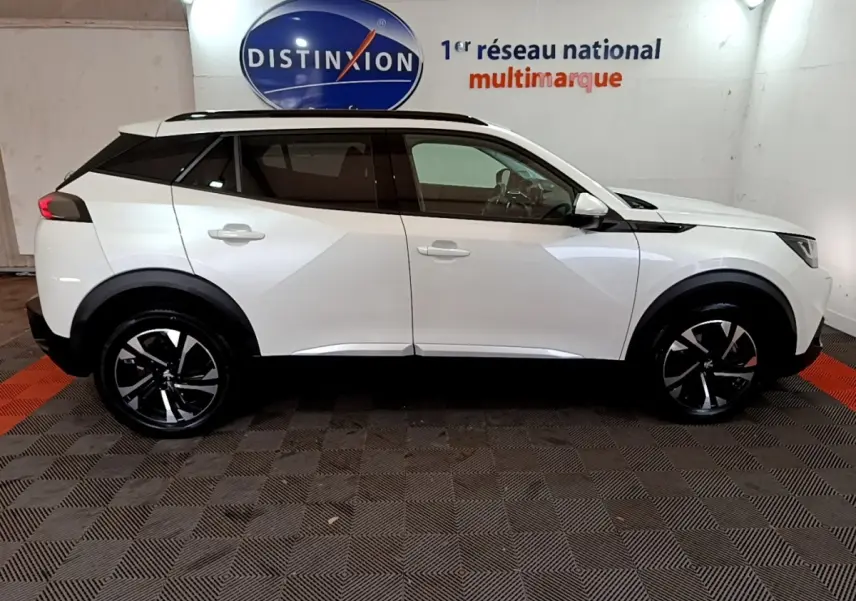 Vue de profil côté gauche d'un Peugeot 2008 blanc 2021 avec jantes noires et toit noir, dans un showroom intérieur.