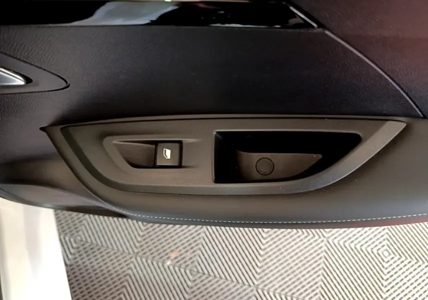 Gros plan sur la commande de lève-vitre côté gauche de la porte intérieure noire d’un Peugeot 2008 blanc.