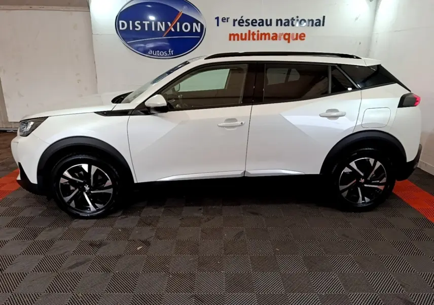 Vue de profil côté gauche d'un Peugeot 2008 blanc 2021 avec jantes alliage noires et toit noir contrasté.