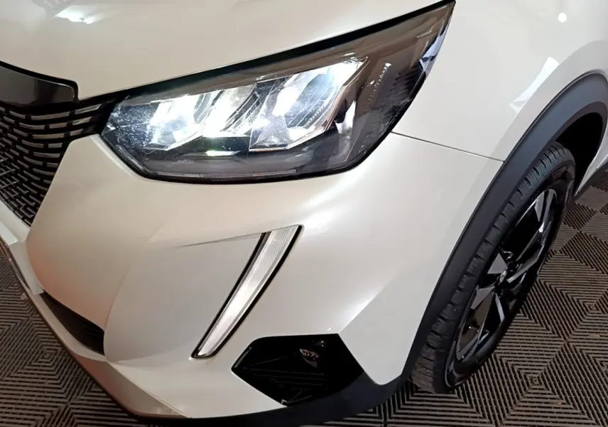 Gros plan sur l'avant droit blanc du Peugeot 2008 2021, mettant en valeur le phare LED et la roue noire brillante.