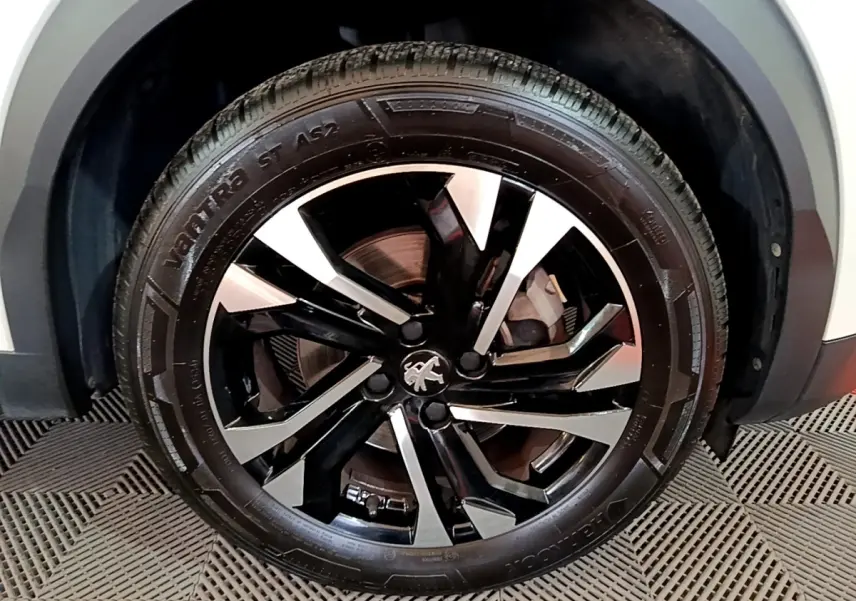 Gros plan sur la roue avant droite du Peugeot 2008 blanc, mettant en valeur la jante alliage noire et argentée au design moderne.