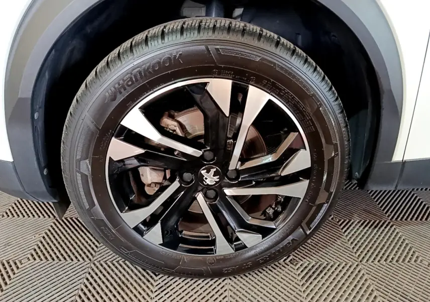 Gros plan sur la roue avant droite d’un Peugeot 2008 blanc, jante alliage noire et argentée au design moderne.