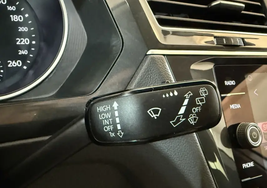 Gros plan sur la commande des essuie-glaces du Volkswagen Tiguan gris clair, avec tableau de bord et écran tactile en arrière-plan.