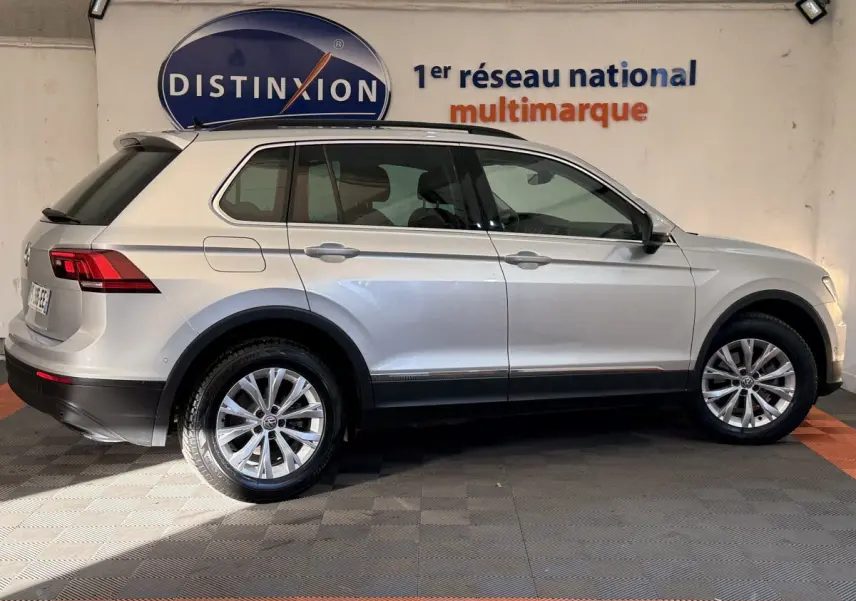 Profil droit d'un Volkswagen Tiguan gris clair 2020 garé en intérieur avec jantes alliage et barres de toit noires.