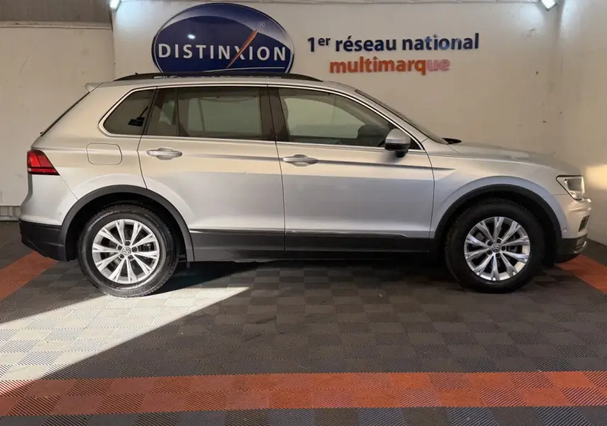 Vue de profil côté gauche d'un Volkswagen Tiguan gris clair garé en intérieur sur sol à damiers, avec logo Distinxion en arrière-plan.