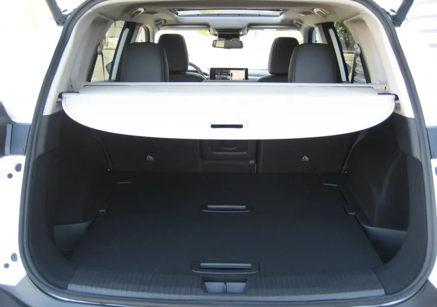 Coffre ouvert vu de l'arrière d'un Nissan X-Trail blanc nacré avec cache-bagages déployé et intérieur noir.