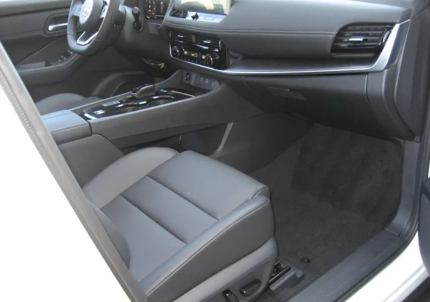 Vue intérieure côté passager du Nissan X-TRAIL blanc nacré, mettant en valeur le tableau de bord moderne et les sièges en cuir gris.