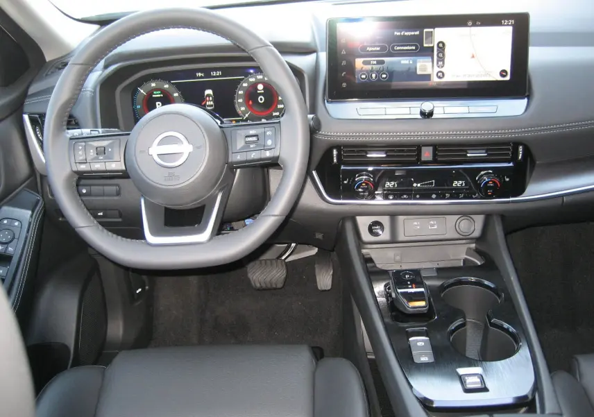 Vue intérieure avant du tableau de bord et volant du Nissan X-TRAIL blanc nacré avec écran tactile et commandes modernes.