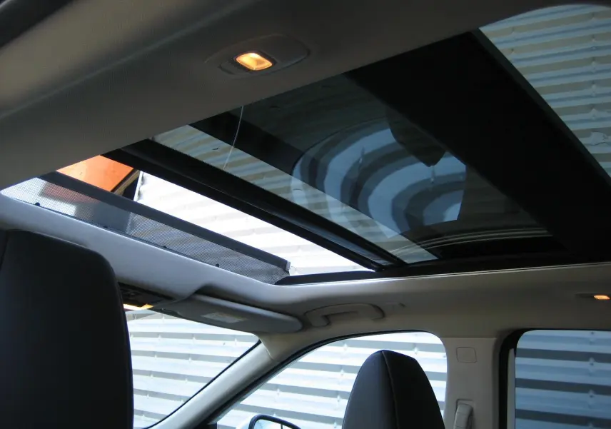 Vue intérieure du toit ouvrant panoramique du Nissan X-TRAIL blanc nacré, avec sièges avant et lumière intérieure allumée.
