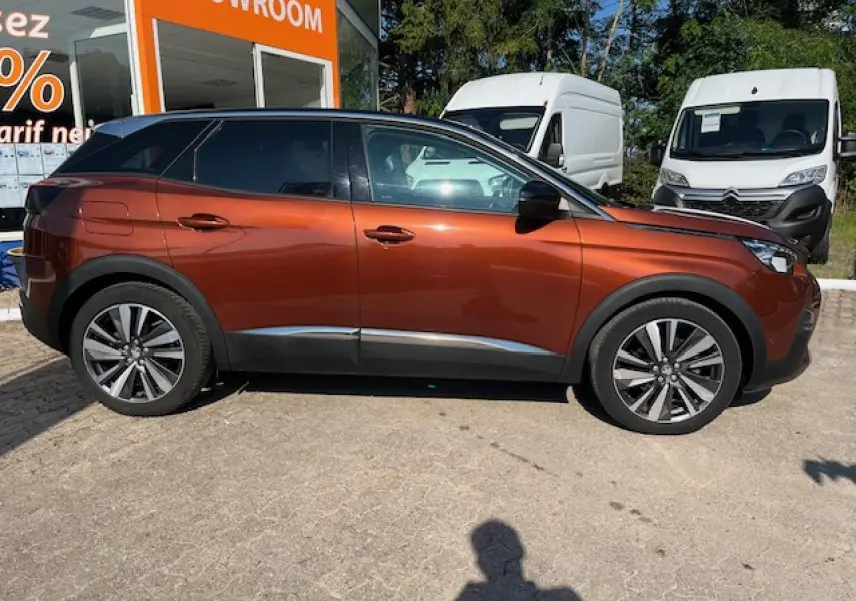 Profil côté gauche d'un Peugeot 3008 2016 métallisé cuivre avec jantes alliage, garé devant un showroom.