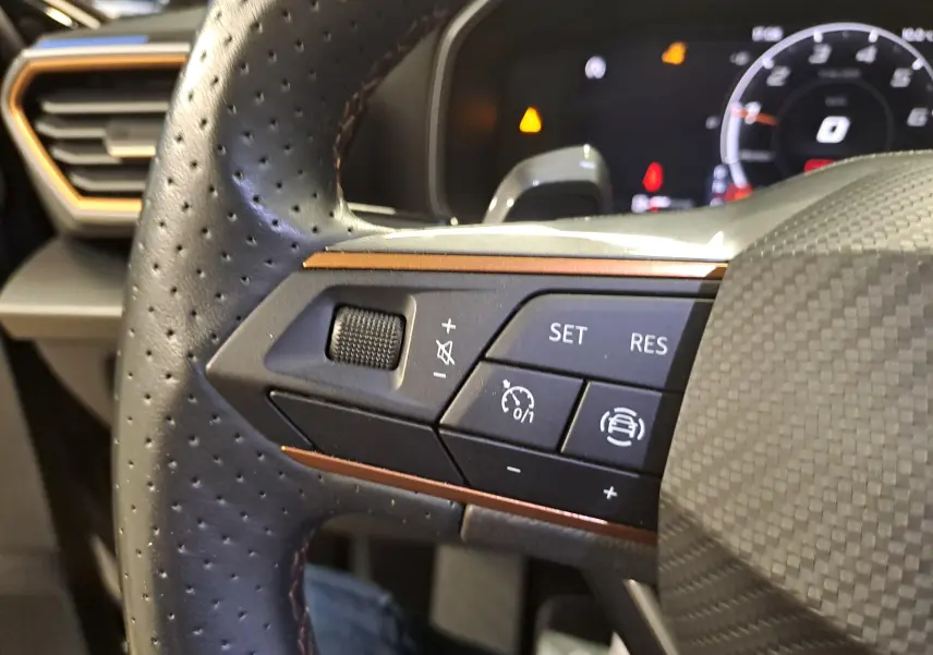 Détail du volant perforé avec commandes de régulateur sur la gauche d'une CUPRA Leon 2023 Noir Minuit.