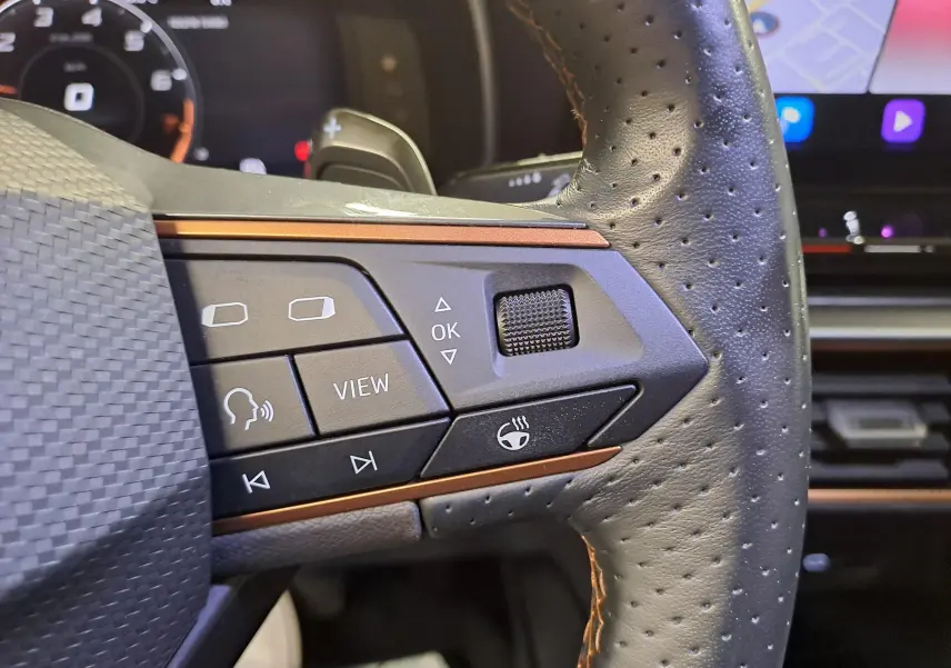 Gros plan sur les commandes gauche du volant perforé noir avec surpiqûres cuivrées du CUPRA Leon 2023.