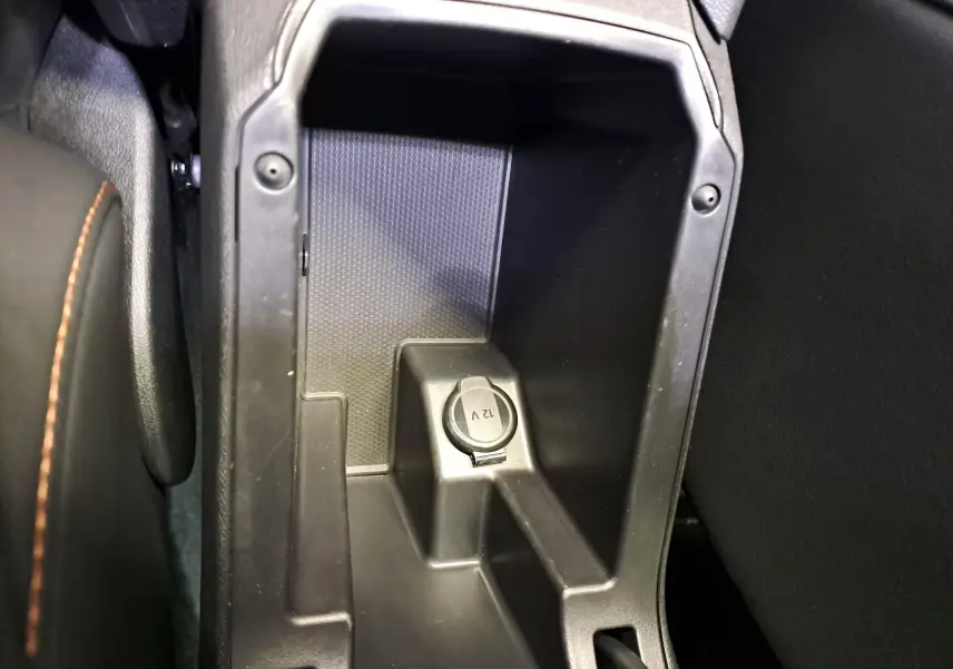 Prise 12V dans le rangement central intérieur du CUPRA Leon 2023 Noir Minuit, vue rapprochée du compartiment entre sièges.