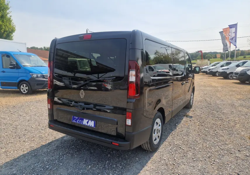 Vue 3/4 arrière droite d’un Renault Trafic Combi noir 2026 avec vitres teintées et hayon fermé sur parking.