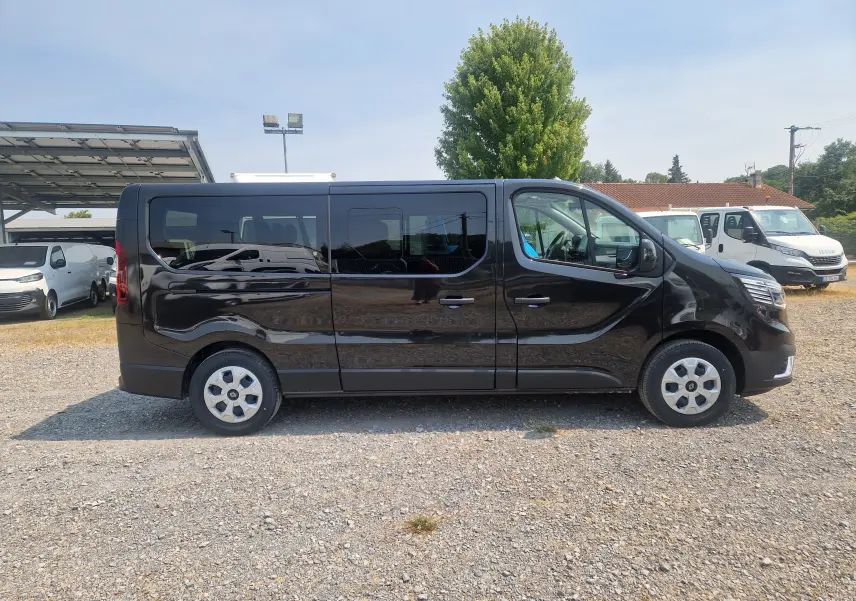 Profil latéral droit d’un Renault Trafic Combi noir 2026, avec vitres teintées et jantes acier, stationné sur un sol gravillonné.