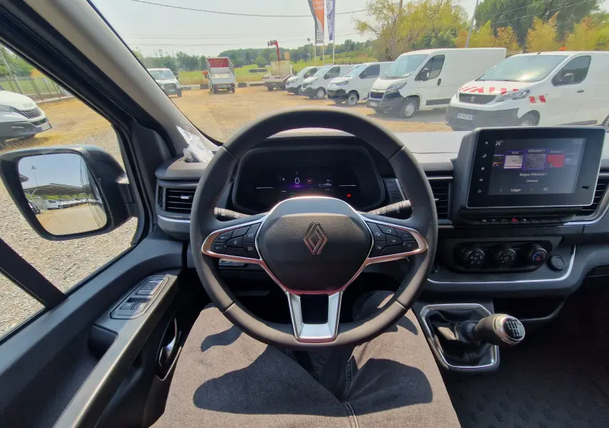Vue intérieure centrée sur le volant du Renault Trafic Combi noir, avec tableau de bord digital et levier de vitesses manuel visible.