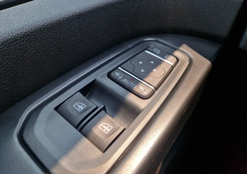 Gros plan sur les commandes de lève-vitres et réglage des rétroviseurs côté conducteur du Renault Trafic Combi noir.
