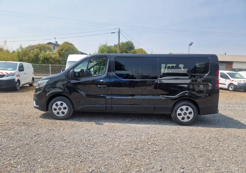 Vue de profil côté gauche d’un Renault Trafic Combi noir 8 places avec vitres teintées sur un parking extérieur.