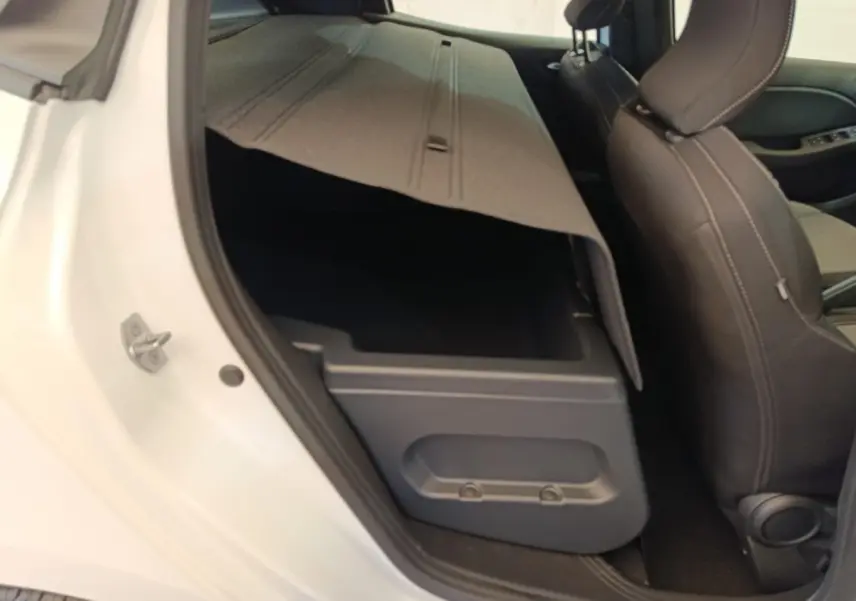 Vue intérieure côté gauche arrière de la Renault Clio blanche 2024 avec banquette rabattue et coffre de rangement visible.