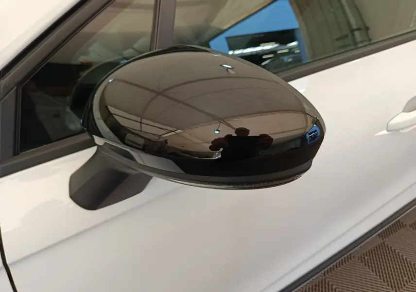 Rétroviseur noir brillant côté conducteur d'une Renault Clio blanche vue de près sur fond intérieur.
