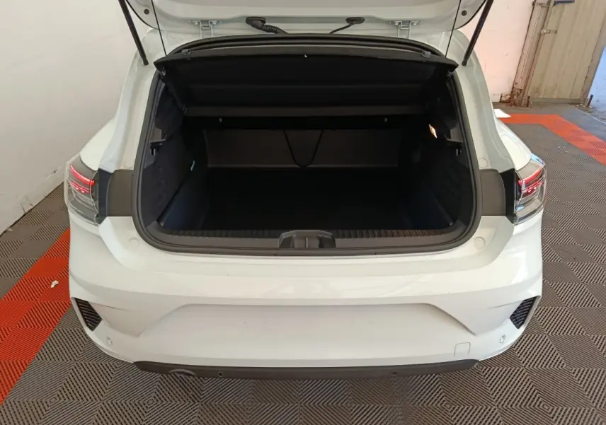 Vue arrière ouverte du coffre d'une Renault Clio blanche 2024, avec feux arrière LED visibles et intérieur de coffre spacieux.