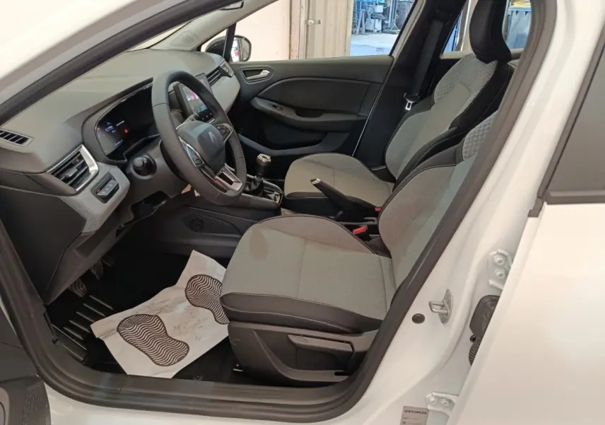 Intérieur de la Renault Clio blanche 2024 vu côté conducteur, montrant sièges gris et tableau de bord moderne.