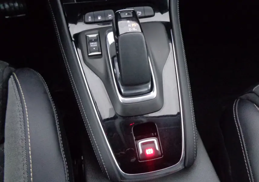 Gros plan sur la console centrale noire brillante de l'Opel Grandland X hybride, avec levier de vitesse automatique et frein à main électronique.