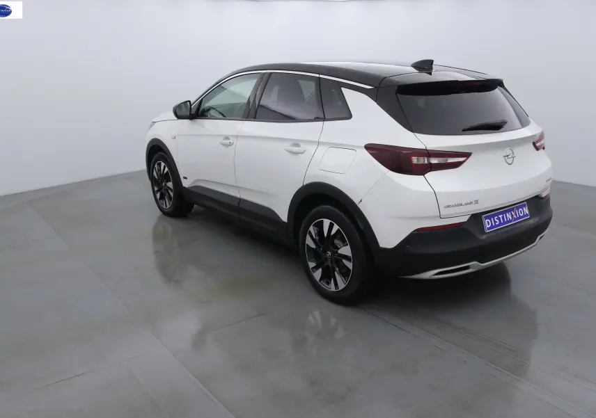 Opel Grandland X blanc métal vue 3/4 arrière droit avec toit noir et jantes bicolores en studio.