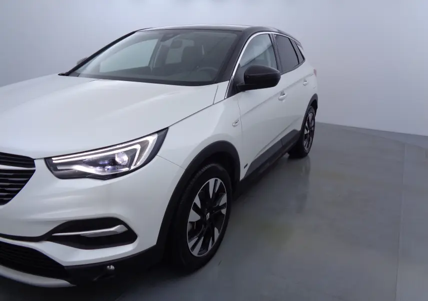 Vue 3/4 avant droit d'un Opel Grandland X blanc métal avec toit noir et jantes bicolores dans un studio lumineux.
