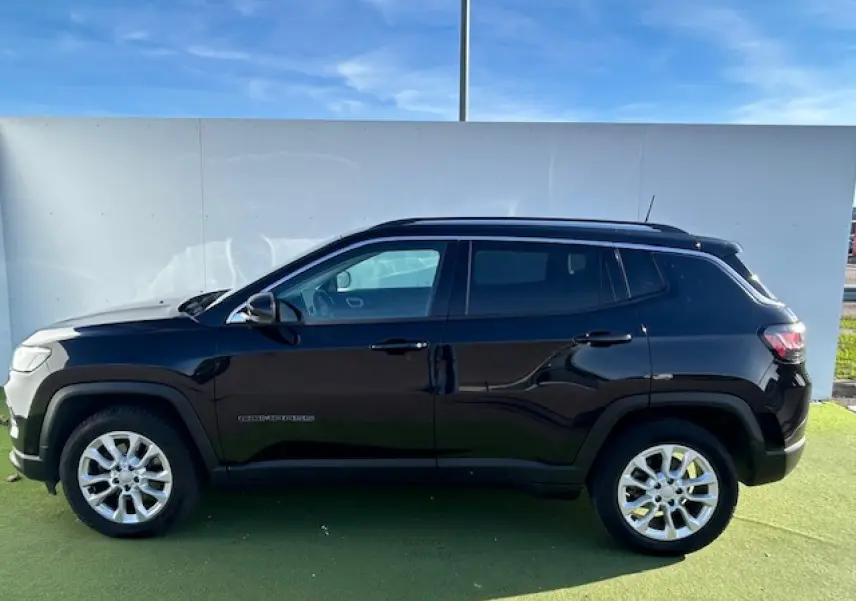 Jeep Compass noir métallisé vu de profil côté gauche, avec jantes alliage 17 pouces et barres de toit longitudinales.