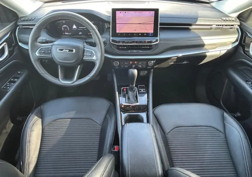 Vue intérieure avant du Jeep Compass noir, mettant en valeur le tableau de bord numérique et la console centrale avec écran tactile.