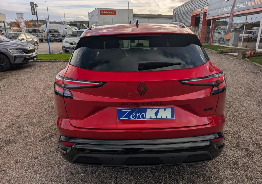 Vue arrière d'un Renault Austral rouge métallisé avec logos noirs et hayon fermé sur un parking extérieur.